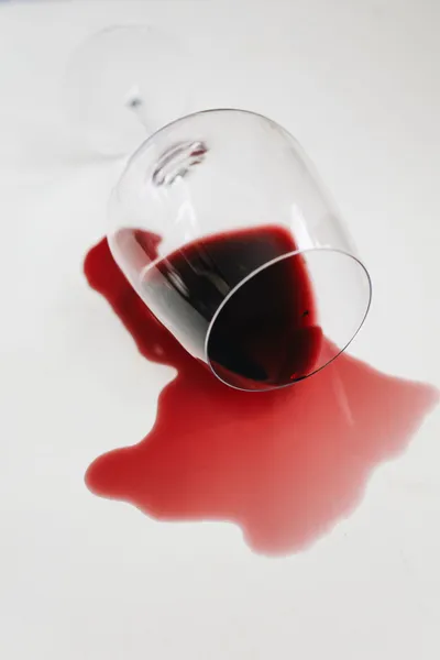 Verre de vin rouge renversé et flaque de vin sur une surface blanche