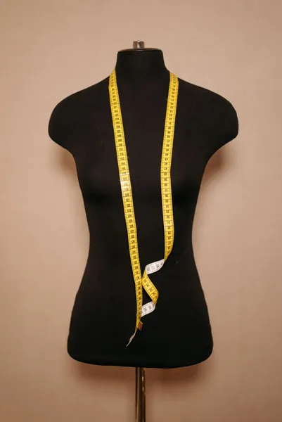 Mètre ruban jaune de couturière passé autour du cou d’un buste de mannequin noir