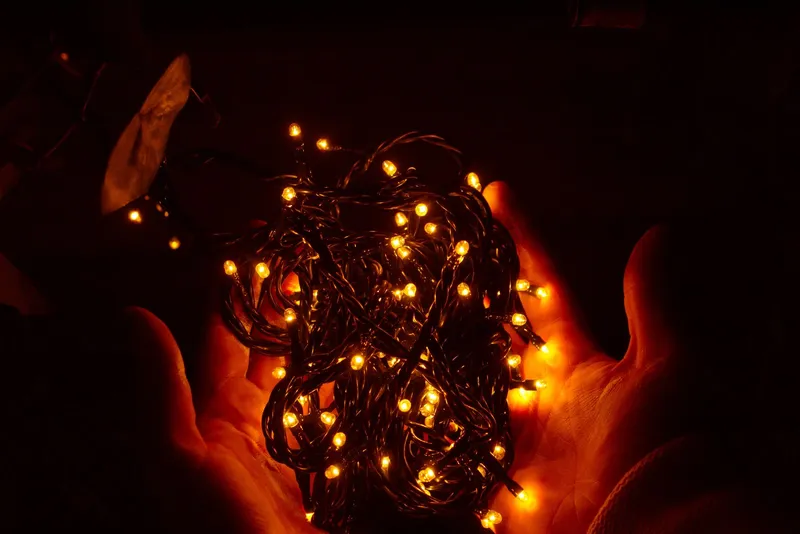 Guirlande de petites LED allumées, emmêlée dans deux mains ouvertes, sur fond noir