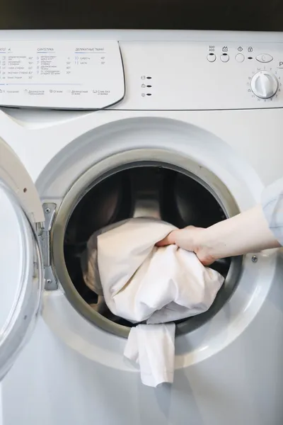 Main qui glisse du linge blanc dans le tambour d'un lave-linge à hublot