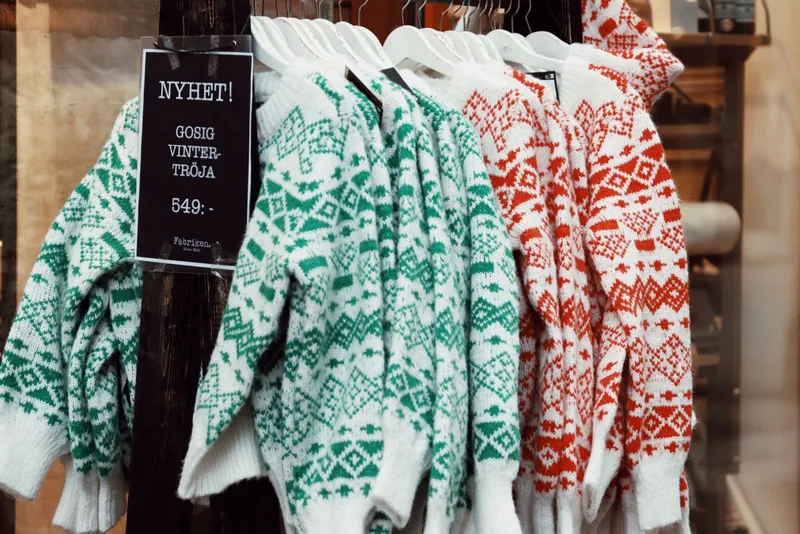 Pulls jacquard verts et rouges sur cintres blancs dans une boutique suédoise, sous une affichette de prix « 549:- »