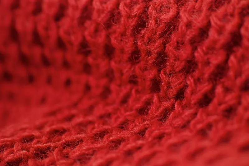 Gros plan sur une maille de laine rouge d’où dépassent de fines fibres duveteuses
