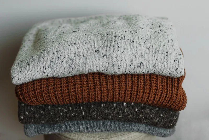 Quatre pulls en laine pliés et empilés : gris moucheté, rouille côtelé, gris anthracite et bleu-gris