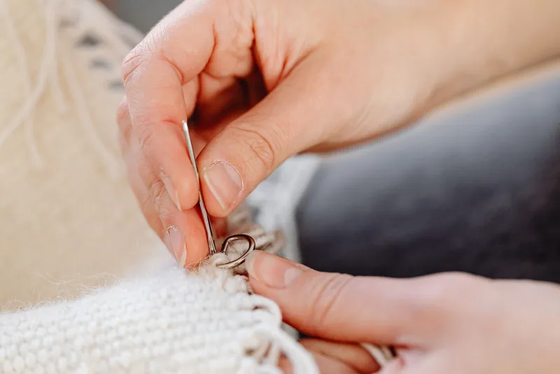 Mains qui travaillent à l'aiguille le bord d'un tricot de laine écrue