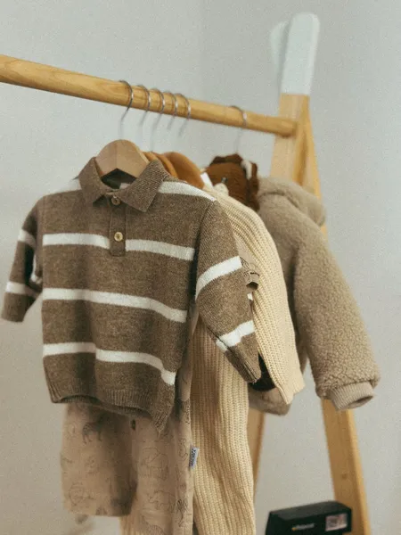 Petits vêtements d'enfant sur cintres : polo en maille marron rayé de blanc, pull crème côtelé et veste en bouclette