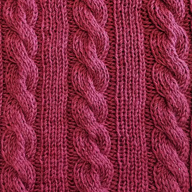 Trois torsades en relief sur un tricot framboise, séparées par des colonnes de côtes